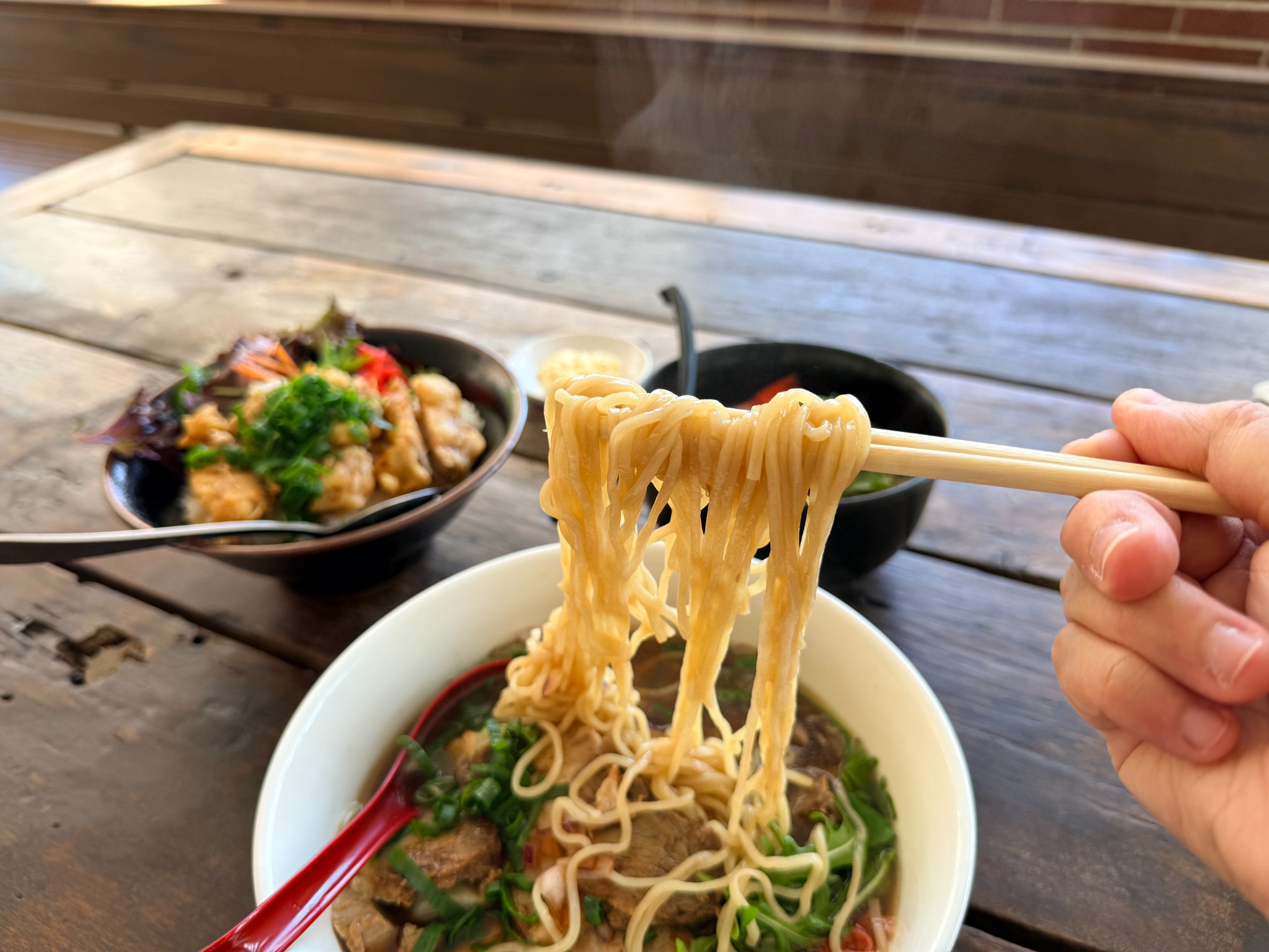 Noodles being lifted with chopsticks from a bowl served at Fat Fish Ramen